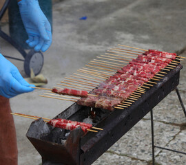 cook with latex gloves cooking raw skewers with mutton and lamb called ARROSTICINI a typical dish...