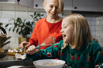 Mother and daughter baking holiday treats and having fun together, Christmas traditions, family bonding, festive kitchen, joyful cooking, winter holiday fun.