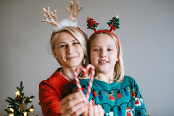 Mother and daughter holding heart-shaped candy canes. Celebrating family warmth, Christmas traditions, holiday moments, cozy gatherings, festive cheer.