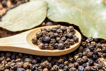 Dry spice black peppercorns on a wooden spoon and dried bay leaf. Spices and seasonings, cooking