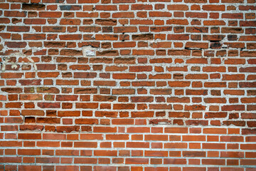 A close-up of a weathered brick wall with a mix of red and brown hues. The bricks are uneven and have a rough texture.