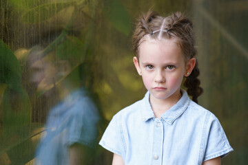 Little sad girl with two big pigtails near the glass. Concept of sad childhood