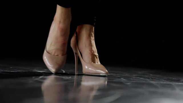 Woman performs a captivating tap dance routine on stage, showcasing her high heels and black pants against a dark background. The performance highlights her skill and elegance