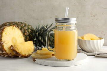 Tasty pineapple juice in mason jar and fresh fruits on white wooden table against grey background, closeup
