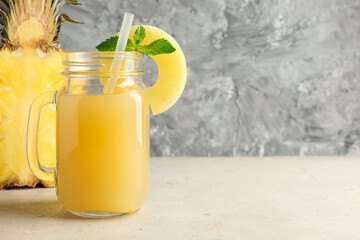 Tasty pineapple juice in mason jar, mint and slice of fresh fruit on grey textured table, closeup. Space for text