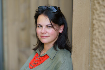 Beautiful dark-haired European woman in her thirties poses for a portrait photo in a khaki linen shirt and coral beads. Concept of natural female beauty