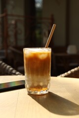 Glass of refreshing iced coffee and straw on wooden table outdoors