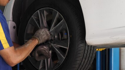 Auto mechanic wearing gloves changing car tire on lift in garage, car maintenance and repair.