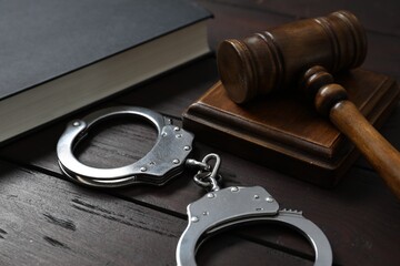 Handcuffs, judge's gavel and book on wooden table, closeup