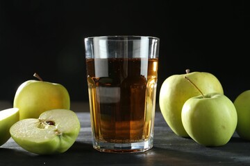 Tasty fresh apple juice in glass and fruits on black wooden table, closeup