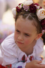 Close-up photo of a cute little girl in a traditional Ukrainian embroidered shirt and a wreath on her head. Concept of unity of traditions and generations