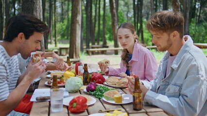 Laughing group eating picnic table in summer forest closeup. Relaxed youngsters