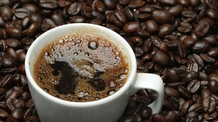 Close up of aromatic hot coffee bubble in to cup with black background. Hot coffee or espresso is pouring into white coffee cup falling into boiled water with separated black backdrop. Comestible.