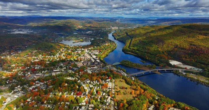 Splendid scenery of an inhabited area located near the river and mountains. Aerial perspective on the panorama of Vermont, New England, USA in autumn. Dramatic cloudscape in the sky.