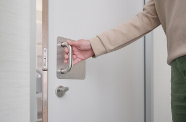 Hand of an unrecognizable woman pulling the handle of the sliding door to open and exit the bathroom of a hospital room