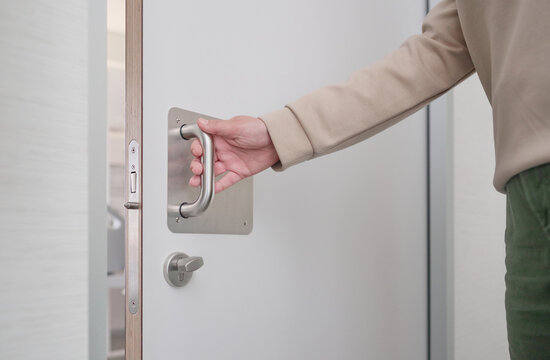 Hand of an unrecognizable woman pulling the handle of the sliding door to open and exit the bathroom of a hospital room