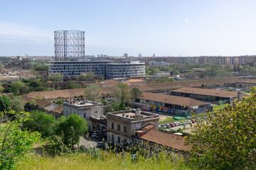 Panoramic view of the Ostiense district in Rome, with the famous Gasometer dominating the skyline. In the foreground, the former Mattatoio di Roma, built in the 19th century
