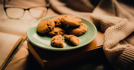 During a cozy reading session with an old book, a plate of homemade chocolate cookies is served to refresh the reader. A rest and a delicious meal. Hygge.