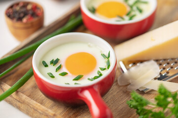 Oeuf cocotte. Baked eggs (Eggs in cocotte) with сheese and green onion in portion ceramic bowl on white background. Comfort food for breakfast