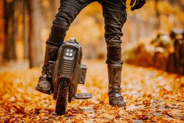 A detailed shot of an electric unicycle and rider’s boots on a forest path, surrounded by fallen autumn leaves. The scene is warm and rustic. © Raivo