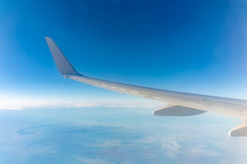View from the airplane window at a beautiful blue clear sky, earth, sea and the airplane wing