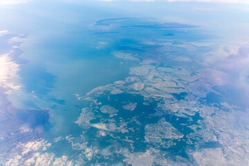 View from the airplane window at a beautiful blue clear sky, earth, sea and the airplane wing