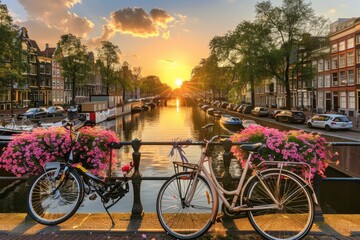 Two bicycles with vibrant flower arrangements rest on a bridge, overlooking a tranquil canal in Amsterdam at sunset, creating a beautiful urban scene.