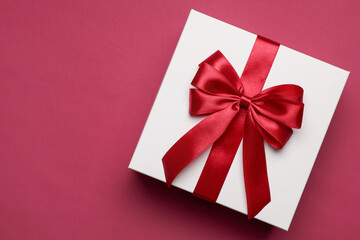 Gift box with red bow on burgundy background, top view. Space for text