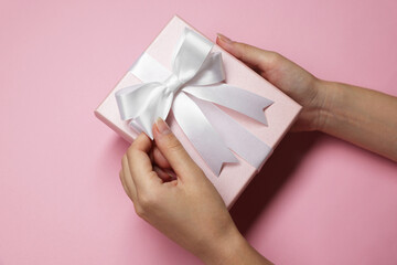 Woman decorating gift box with bow on pink background, top view