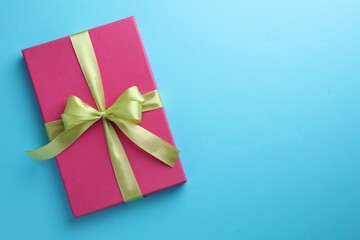 Gift box with bow on light blue background, top view. Space for text