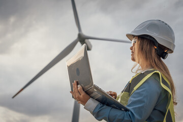 A skilled female engineer monitors wind turbines on her laptop, crucial in developing sustainable energy solutions and advancing technology and infrastructure for a cleaner future