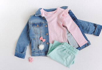 T-shirt with sleeves, denim jacket, shorts and hair accessories on the white background. Set of kids clothes for spring or summer. Flat lay, top view