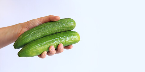 Cucumbers in a woman's hand on a light background. Close-up of a hand with a cucumber. Harvest. Concept of healthy eating and diet. Vegetables. White female hand shows a fresh tasty cucumber