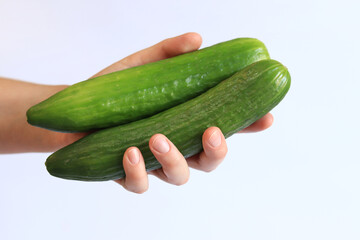 Cucumbers in a woman's hand on a light background. Close-up of a hand with a cucumber. Harvest. Concept of healthy eating and diet. Vegetables. White female hand shows a fresh tasty cucumber