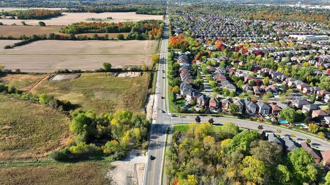 Urban sprawl depicted by an aerial view of a drone flying along a divide between farm land after the autumn harvest and the adjacent suburban neighbourhood.