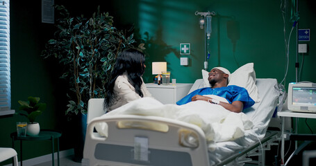 African girl by her boyfriend's side in the hospital, holding hands.