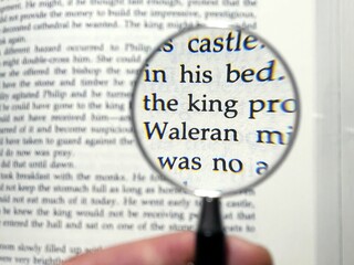 Photo of the phrase “the king” magnified by a magnifying glass in a book written in English