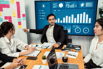 Diverse group of business analyst team analyzing financial data report. Finance data analysis chart and graph dashboard show on TV screen in meeting room for strategic marketing planning. Habiliment