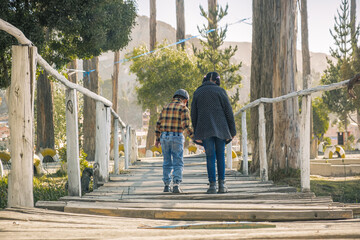 two latin children walking together on a wooden bridge with trees around them in bolivia -...