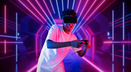 Teenager holding joystick and wearing VR goggles while enjoy playing games at neon abstract background. African man enjoy controlling controller and using augmented reality technology. Ingenuity.