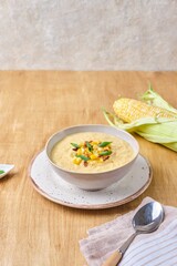 Corn soup puree in beige bowl with corn kernels and spices topping on wooden background. Recipes corn.