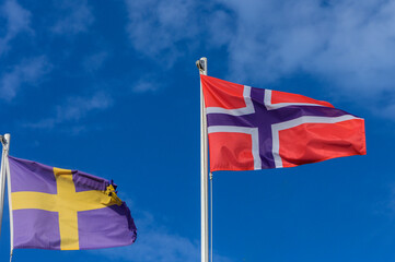 Colorful flags of Sweden and Norway waving against a bright blue sky in a lively summer breeze