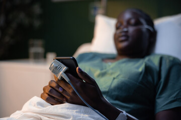 Girl from Africa, tubes in her nose and an oxygen meter on her finger, shares a smile over a phone...