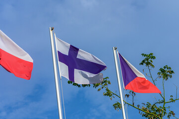 Colorful flags of Finland, Poland, and the Czech Republic waving peacefully against a bright blue sky in a serene outdoor setting