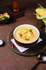 Corn soup puree in a dark bowl with corn and spice topping on a brown concrete background. Recipes corn. Seasonal products. Thanksgiving day
