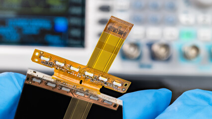 Close-up a mobile phone flex printed circuit with flat cable in repairman hand. White LED diodes for LCD display backlight and small surface mounted electronic components on FPC from cellphone inside.