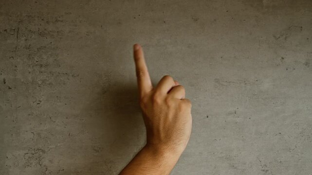 Man's hand pointing upward with index finger against rough concrete wall in simple minimalist setting
