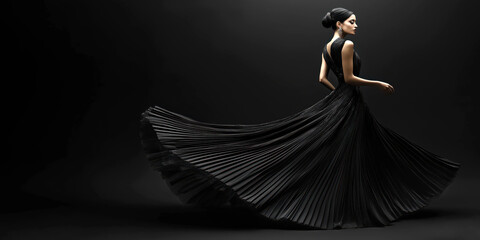 Fototapeta premium Elegant woman in black evening dress posing against dark background in studio