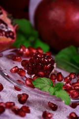 Red pomegranate on a gray background. Whole and pieces. Ripe pomegranate seeds on a glass plate. All mint leaves.