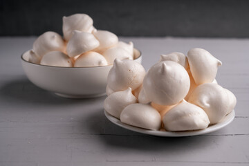 The image shows two plates of meringue cookies. They are white, light, and airy in appearance. Meringues are typically made from whipped egg whites and sugar